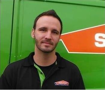A man with a back polo on standing in front of a SERVPRO vehicle.