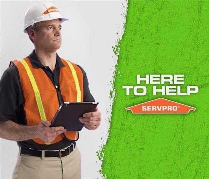 Man standing with SERVPRO hardhat on and iPad in hand, and text on graphic that reads Here to Help